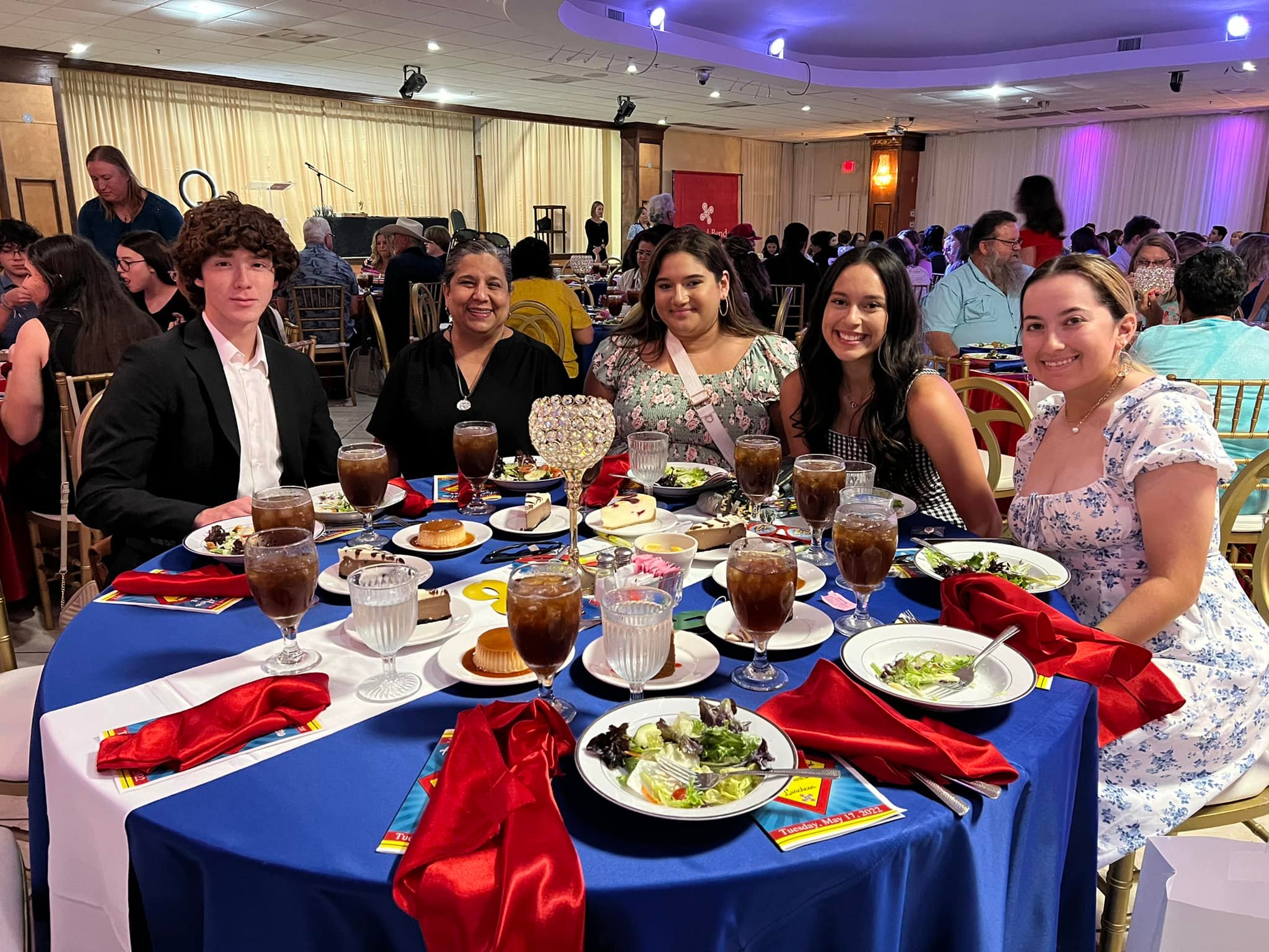 Group at a table with food and drinks with a large amount of people in the back
